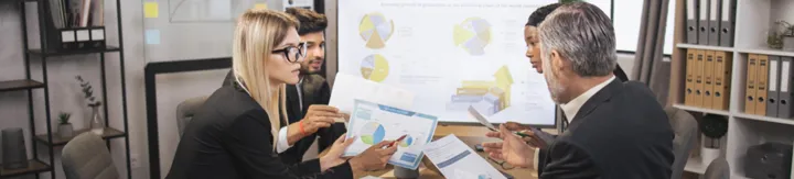 Four diverse professionals discussing charts and graphs during a business meeting in an office.
