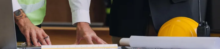 Two professionals reviewing architectural plans on a table with a yellow safety helmet and walkie-talkie.