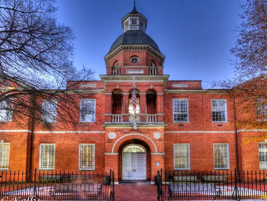 Historic red brick building with central tower and American flag, clear blue sky.