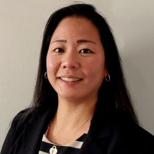 Professional headshot of a woman with long black hair wearing a black blazer and striped top.