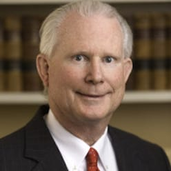 Portrait of an older man with white hair in a suit and red tie, library background.