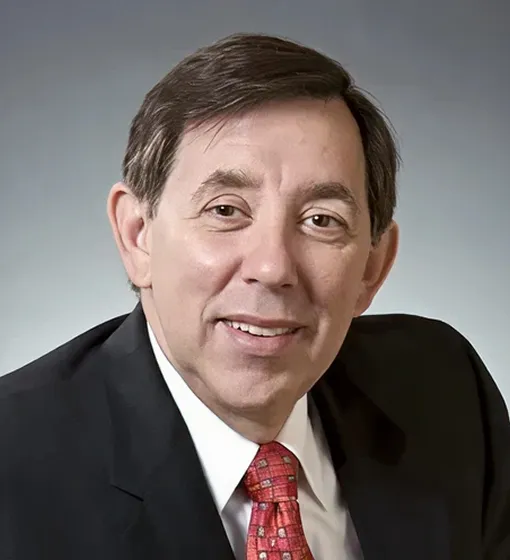 Portrait of a middle-aged man in a black suit, white shirt, and red patterned tie against a gray background.