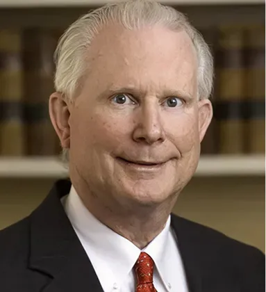 Portrait of an older man with white hair wearing a black suit, white shirt, and red tie.