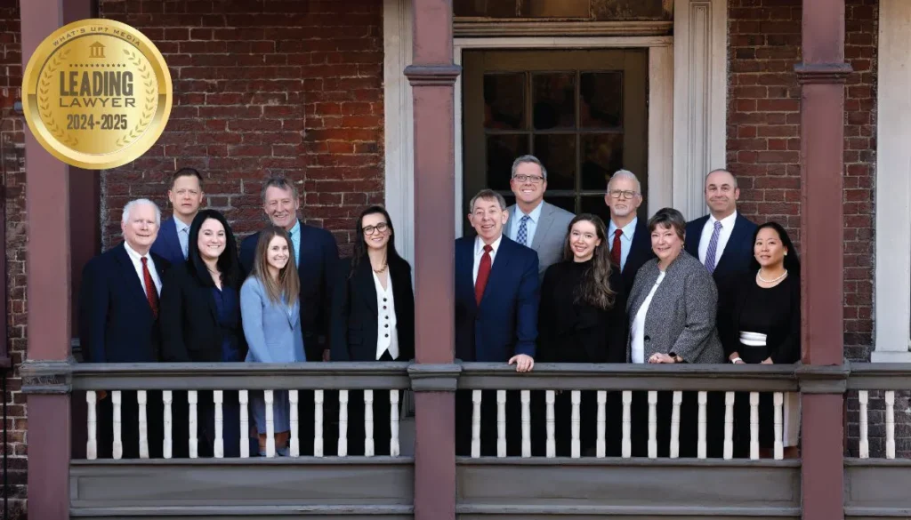 Group portrait of fourteen professionally dressed individuals standing on a brick balcony, with a "Leading Lawyer 2024-2025" gold seal in the top left corner.