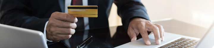 Person in formal attire holding a gold credit card and using a laptop keyboard.