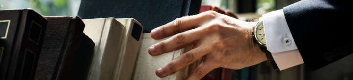 Close-up of a hand in a suit sleeve selecting a book from a shelf with sunlight.