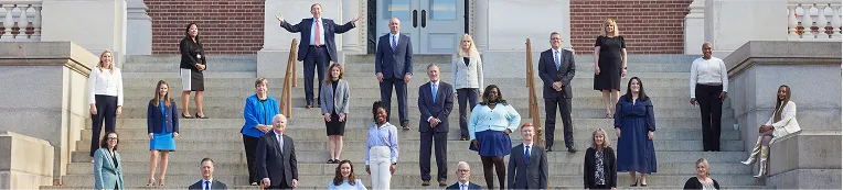Group of professionally dressed individuals standing on stone steps outside a large building with columns.