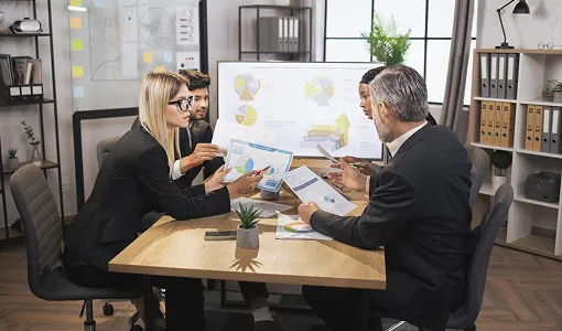 Four business professionals engaged in a meeting, reviewing charts and documents in a modern office.