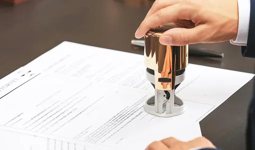 Hand pressing a gold and black self-inking stamp on a document with printed text.