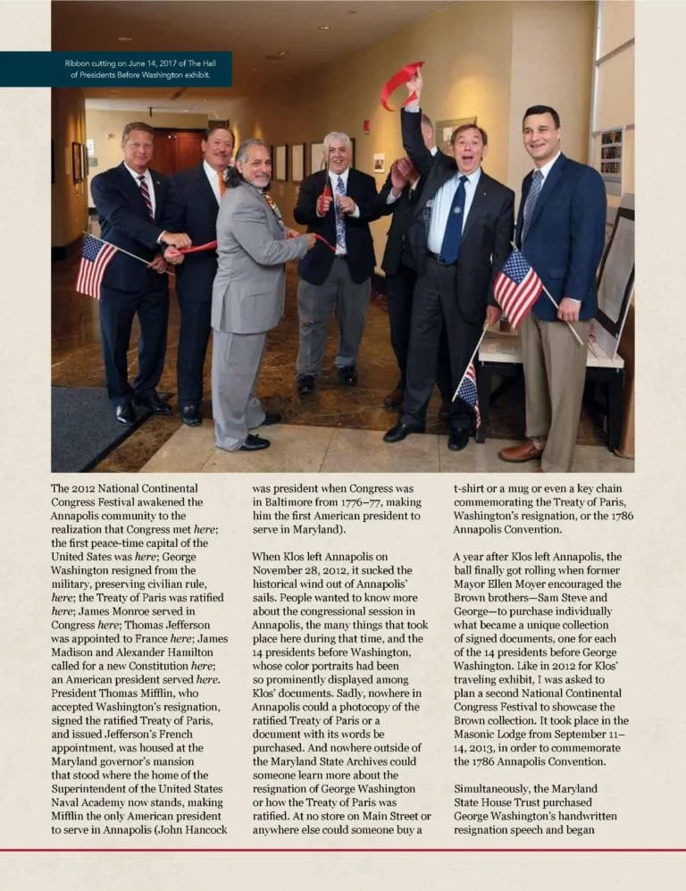 Seven men in formal attire participate in a ribbon-cutting ceremony indoors, two holding American flags.