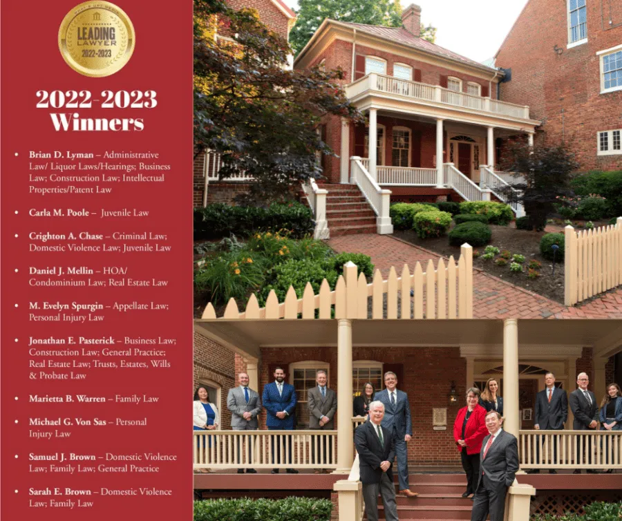 Group of professionally dressed individuals standing on porch of a large brick building with white picket fence and landscaped garden.