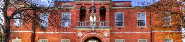 Front view of a red brick institutional building with white-trimmed windows and an American flag.
