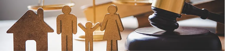 Wooden figures of a family and house next to a judge's gavel on a desk.