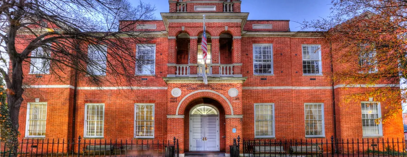 Red brick courthouse building with white doors, American flag, and leafless trees.