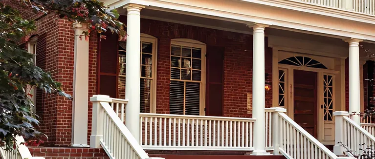 Brick house facade with white columns, railing, and wooden front door.