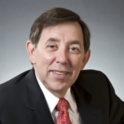 Professional headshot of a middle-aged man in a black suit and red patterned tie.