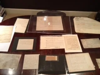 Collection of historical handwritten documents and certificates displayed on a wooden table.