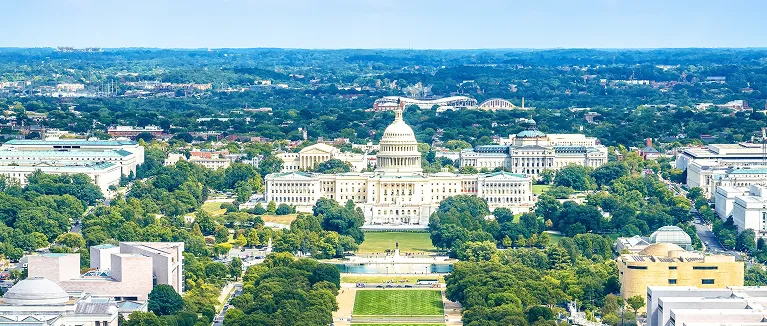 Aerial view of the United States Capitol building surrounded by green trees and urban landscape.
